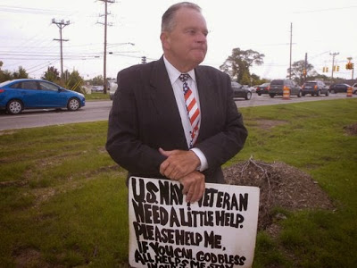 Man in his 50s or 60s dressed in a suit holding a sign reading "U.S. Navy Veteran. Need a little help. Please help me.